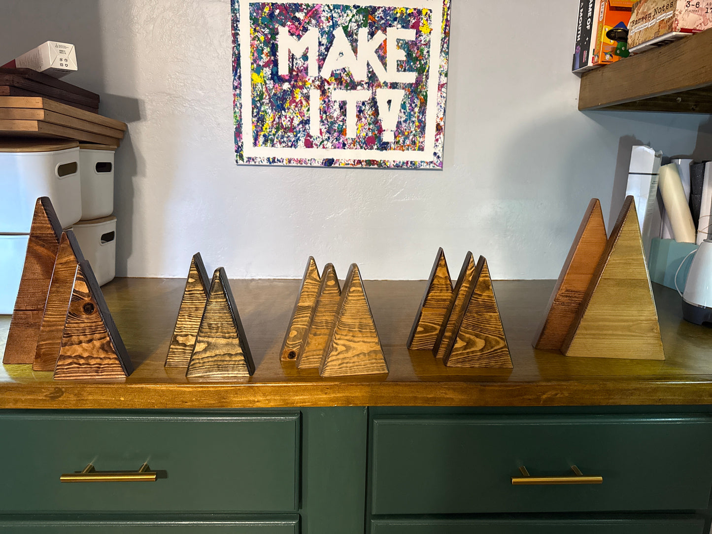 Wooden pyramid-shaped objects on a wooden surface with a colorful 'MAKE IT' poster in the background.