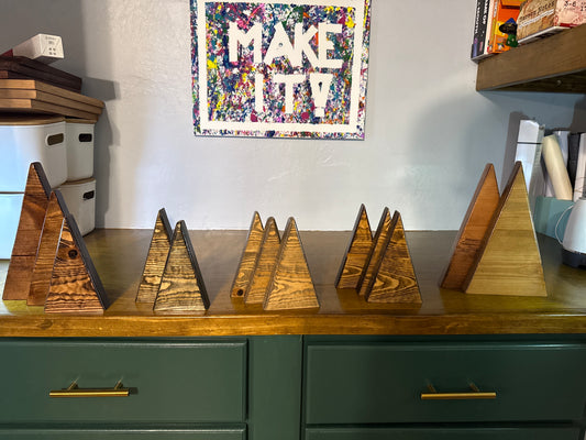 Wooden pyramid-shaped objects on a wooden surface with a colorful 'MAKE IT' poster in the background.